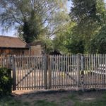 Dubbele franse rondhoutpoort van 120 cm breed bij 120 cm hoog per poortdeel bevestigd aan hekwerk van kastanjehouten palen en halfronde rasterlatten als doorgang naar de oprit bij een huis.