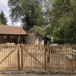 Dubbele franse rondhoutpoort van 120 cm breed bij 120 cm hoog per poortdeel bevestigd aan hekwerk van kastanjehouten palen en halfronde rasterlatten als doorgang naar de oprit bij een huis.