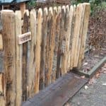 Franse rondhoutpoort van kastanje van 80 cm hoog bij 120 cm breed als doorgang gebruikt in een voortuin.