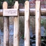 Franse rondhoutpoort van 150 cm hoog met een houten bordje met Adéquat erop gebrand.