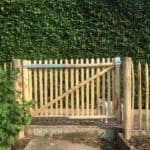 Dubbele Franse rondhoutpoort van 100 cm hoog bij 120 cm breed bevestigd tussen schapenhek van 100 cm hoog als afscheiding in de tuin.