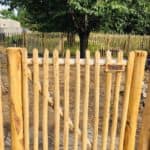 Dubbele Franse rondhoutpoort van 120 cm hoog en 100 cm breed per poortdeel als doorgang naar de tuin met een afscheiding van schapenhek van 120 cm hoog en een latafstand van 8 cm