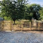Dubbele Franse rondhoutpoort van 120 cm hoog en 100 cm breed per poortdeel als doorgang naar de tuin met een afscheiding van schapenhek van 120 cm hoog en een latafstand van 8 cm