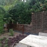 Hazelaarschermen Somme 4 op een stenen verhoging in de tuin als afrastering en privacy scherm