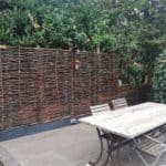 Hazelaarschermen Somme 4 op een stenen verhoging in de tuin als afrastering en privacy scherm