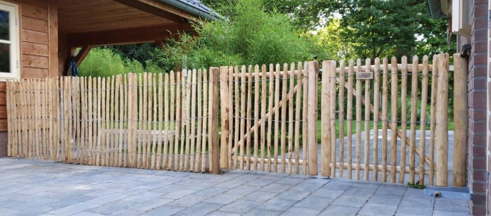 Rasterscherm van 100 cm hoog met latafstand 2 cm tussen twee gebouwen en aan een dubbele raamwerkpoort bevestigd met dezelfde hoogte.