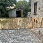 Dubbele franse rondhoutpoort van 150 cm breed bij 100 cm hoog per poortdeel en een looppoortje van 80 cm breed bij 100 cm hoog als doorgang naar een carpoort