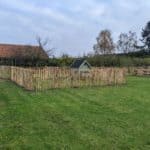 Franse rondhoutpoort van 120 cm breed bij 120 cm hoog als doorgang bij een kippenren omheind met schapenhek an 120 cm hoog met een latafstand van 6 cm