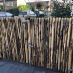 Dubbele Franse rondhoutpoort van 100 cm breed bij 120 cm hoog per poortdeel met de latten tegen elkaar gemonteerd en scharnieren sluiting aan de kant van de latten gebruikt als doorgang naast een huis.
