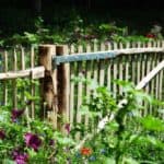 Franse rondhoutpoort van 180 cm breed bij 100 cm hoog geplaats tussen schapenhek in een wilde bloementuin in bloei