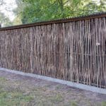 Hazelaarschermen somme 180 gebruikt in de tuin als afrastering bij een afdak waar brandhout ligt opgeslagen.