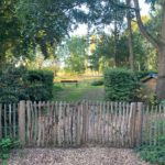 Dubbele Franse rondhoutpoort van 120 cm breed bij 100 cm hoog per poortdeel geplaatst tussen een afrastering van schapenhek in een stuk bos.